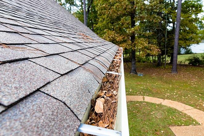 man on ladder removing leaves and buildup from gutter